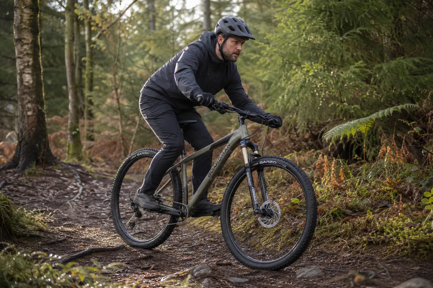 Rider on a grey-green Boardman MHT 8.6 hardtail on British woodland singletrack
