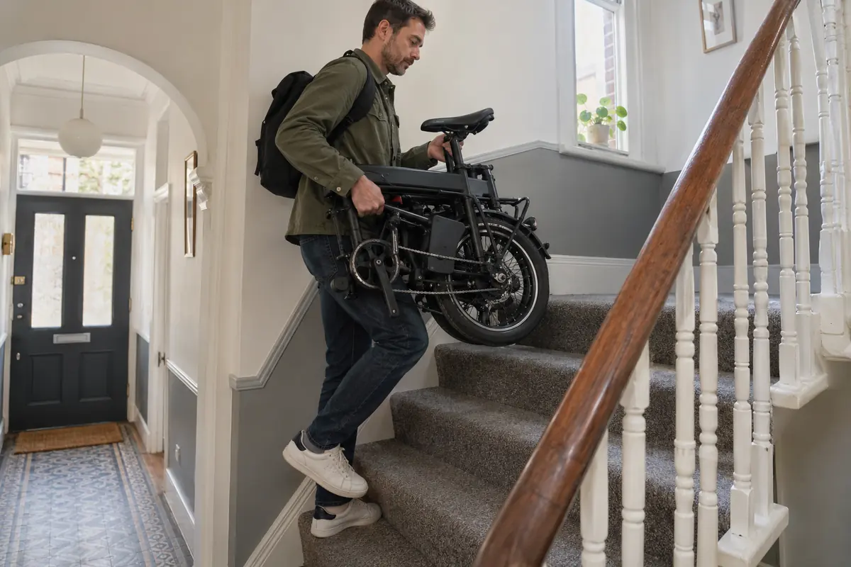 Adult carefully carrying a folded electric bicycle up a narrow flight of stairs