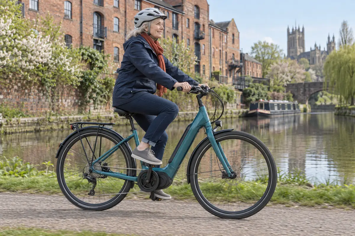 Older woman riding a teal low-step electric bicycle beside a Chester canal