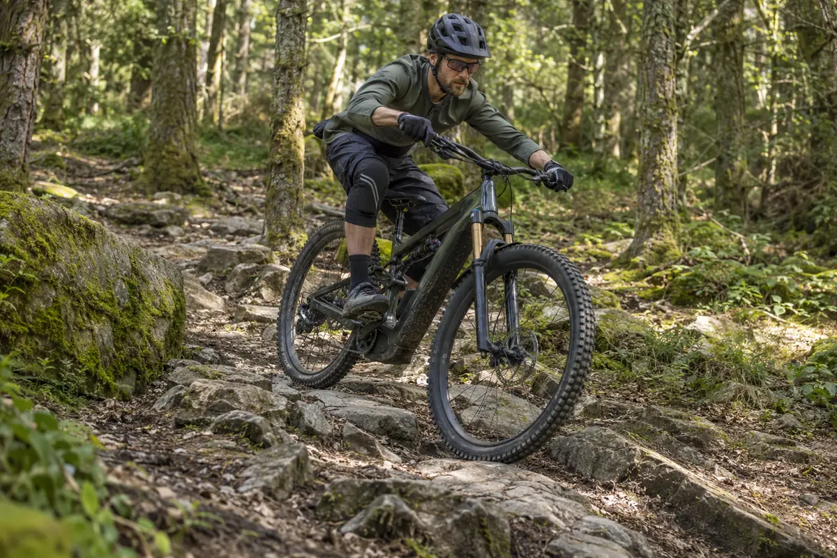 Rider descending a rocky woodland trail on an unbranded electric mountain bicycle